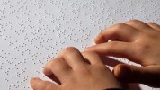 Image qui représente une personne en train de lire une écriture Braille sur papier.